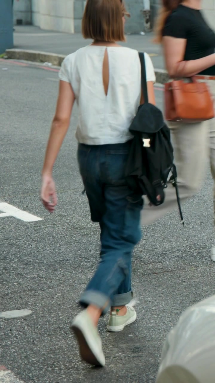 Vertical video: Walking woman in black top olive pants crossing to sidewalk after gap, with bag