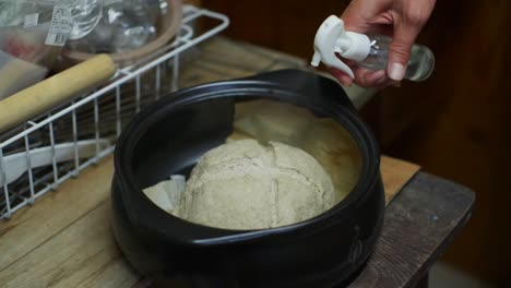 Raw-and-uncooked-ball-of-kneaded-in-black-baking-pot-sprayed-with-water,-filmed-as-closeup-slow-motion-shot