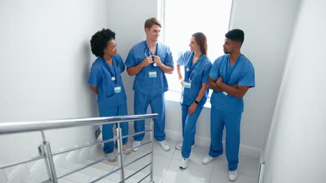 portrait of smiling multi cultural medical team wearing scrubs standing on stairs in hospital