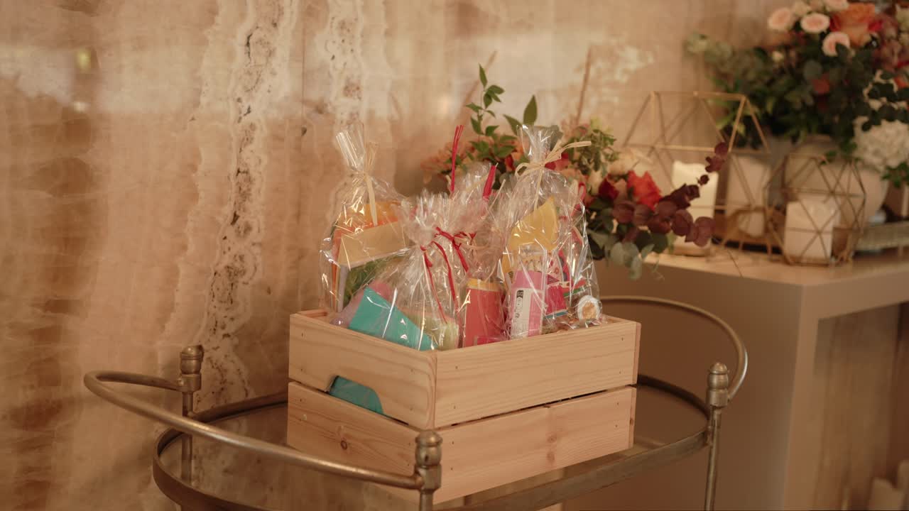 Colorful gift bags in clear wrap displayed in wooden box near floral wedding decor