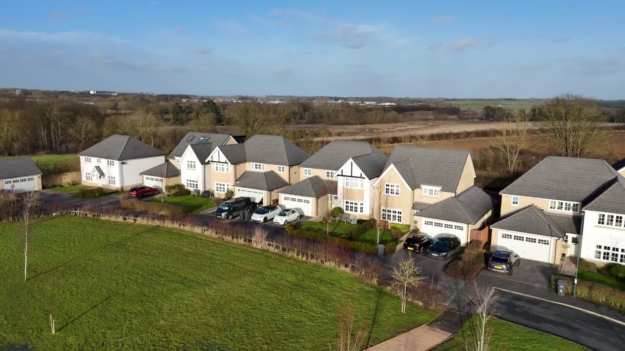 Drone shot shows modern suburban houses in Scotland beside open countryside, with clear skies, green lawns, parked cars, and peaceful quiet surroundings in planned residential area