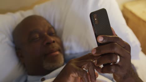 Happy-african-american-senior-man-lying-in-bed-using-smartphone-and-smiling