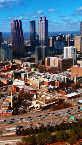 vast scenery of atlanta downtown with few skyscrapers in the middle. lots of cars drive by the wide-lane roads. top view. vertical video
