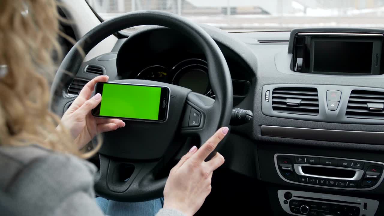여성은 현대 자동차에 앉아 스마트폰으로 작업합니다. 클로즈업 손. 녹색 화면. 크로마 키