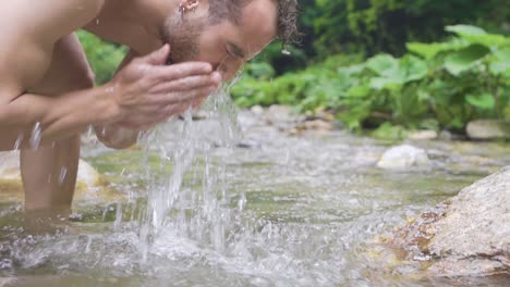 sporty teenager washing face at the creek. slow motion.