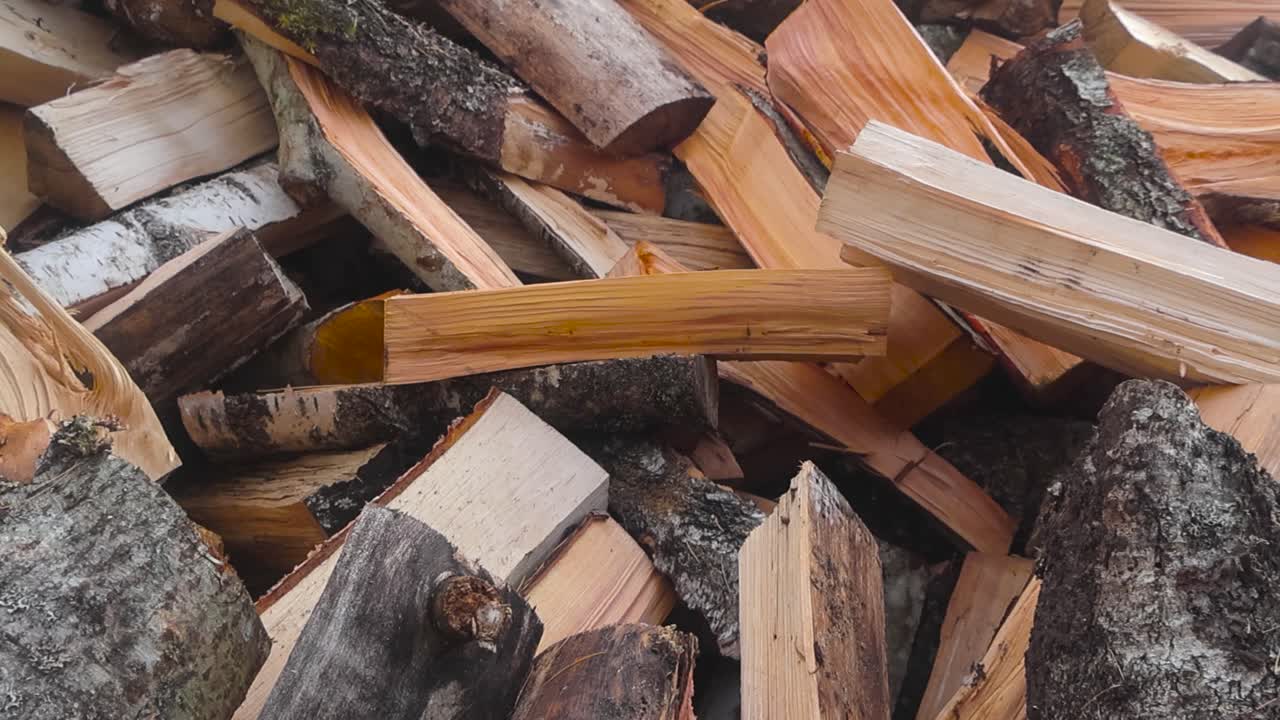 Close up or closeup of a pile of firewood on top of each other on a cloudy day in a garden or a yard during autumn. The wood is broken up and cut revealing the wooden texture of birch and pine trees.