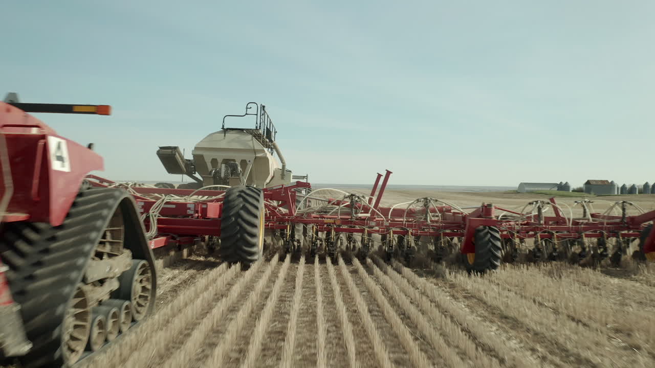 emocionante vuelo de sobrevuelo bajo hacia y por encima de la máquina tractora de siembra de granja roja que viaja en la fila de cultivos de tierras de cultivo en un día soleado, vanguardia, saskatchewan, canadá, acercamiento aéreo