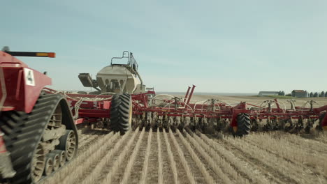 emozionante volo basso cavalcavia verso e sopra la macchina del trattore per la semina della fattoria rossa che viaggia su una fila di colture agricole in una giornata di sole, avanguardia, saskatchewan, canada, approccio aereo ravvicinato