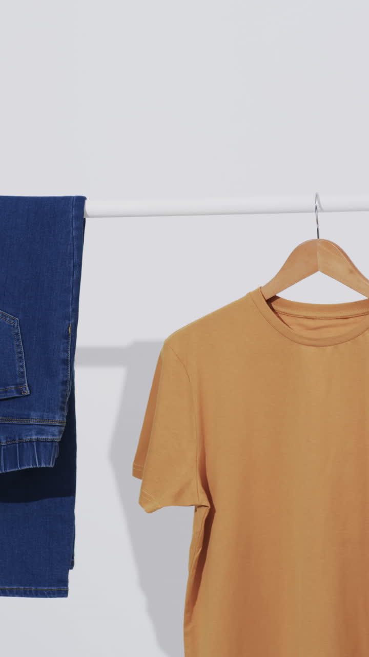 Vertical video of denim jeans and yellow t shirt on hanger and copy space on white background