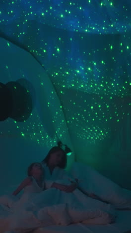 woman with children looks at bright starry sky glowing on ceiling sitting on bed in modern room. dim light source making lighting in premise soft and soothing slow motion