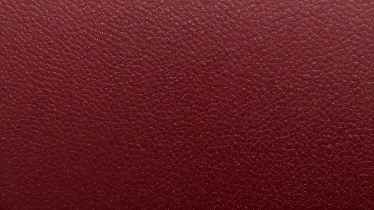 Shifting camera filming lighting shifts on maroon leather panel in studio close up, showing texture