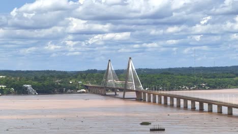 Aerial-wide-shot-showing-boat-and-ship-on-Parana-River-and-San-Roque-González-de-Santa-Cruz-Bridge-during-cloudy-day-with-forest-landscape-in-background