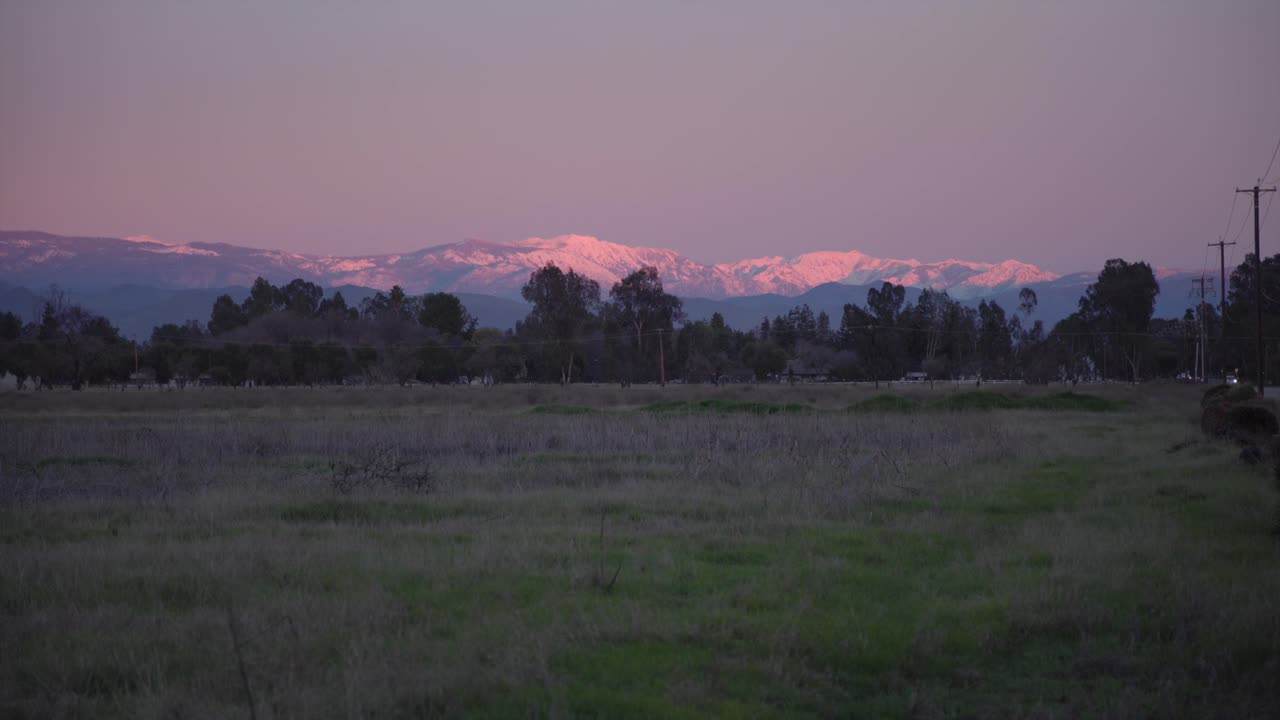 En pastellfarget himmel over Sierra Nevada-fjellene med strømledninger og trær i forgrunnen i Clovis, California, USA.