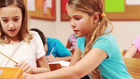 Cute-pupils-working-at-desks-in-classroom