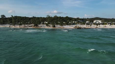 small waves roll over the beautiful white sand beach with huge luxury resorts in the background among the small green trees on the island of koh rong beach
