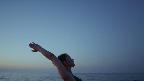 fit girl performing virabhadrasana on beach closeup. woman standing warrior pose