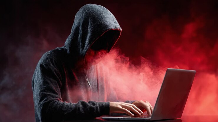 En mystisk skikkelse i en mørk hættetrøje interagerer med en bærbar computer, omgivet af dramatisk rød og sort røg, hvilket fremkalder spænding og intriger