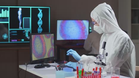 asian doctor in protective suit working on computer in a modern lab. laboratory assistant workplace. the concept of science and medicine