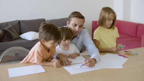 Lächelnder-Vater,-Der-Mit-Kindern-Spricht-Und-Mit-Marker-Auf-Papier-Zeichnet