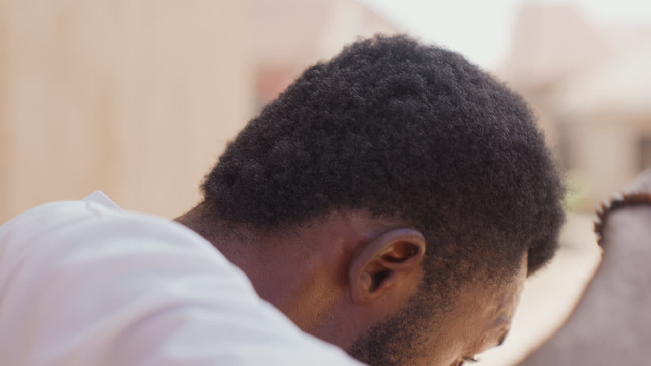 Black athlete tying red headband before training, closeup profile of black man with short afro hair wearing white shirt and beaded bracelet, warm sunlight, focused expression, preworkout grooming