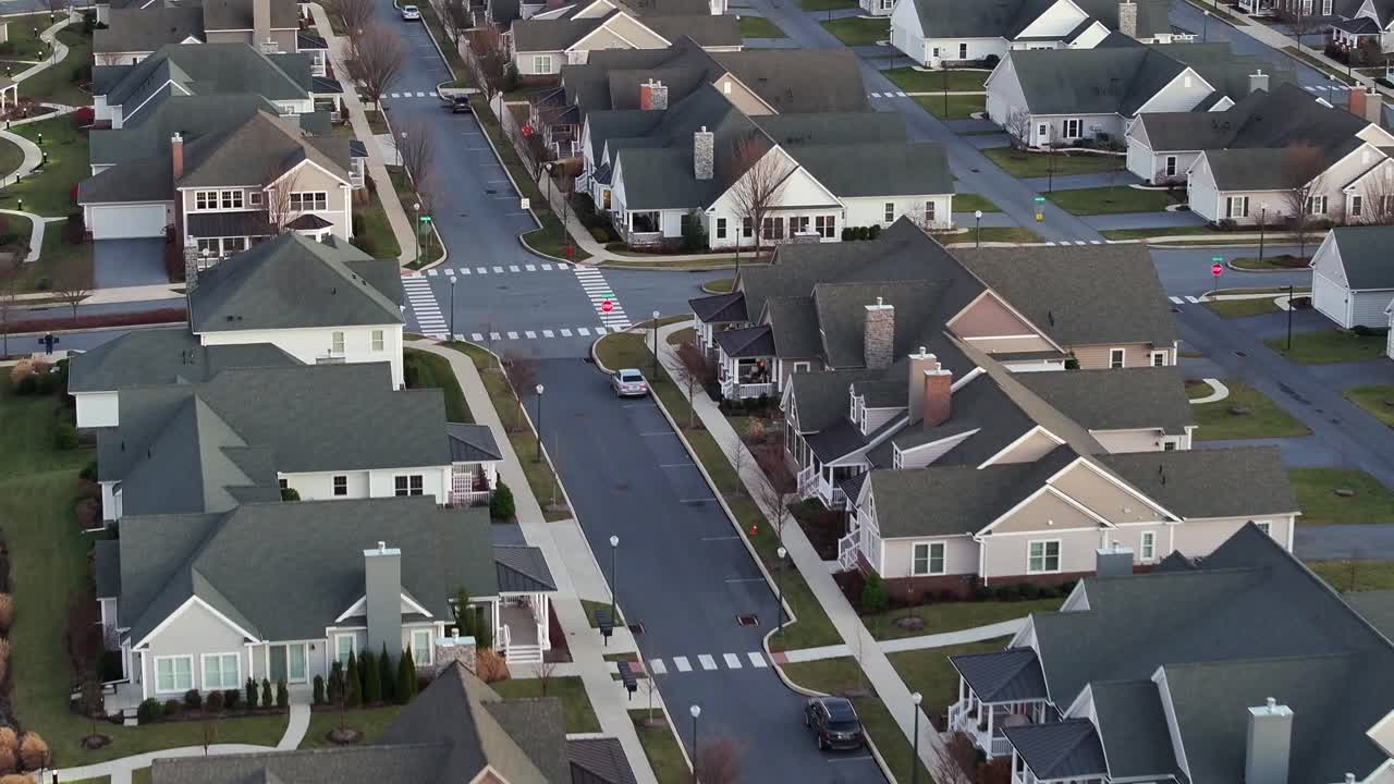 Aerial establishing shot of new build residential area in suburb of american town. Grey rooftops of large homes. Sunset time in winter season. Top down flyover.