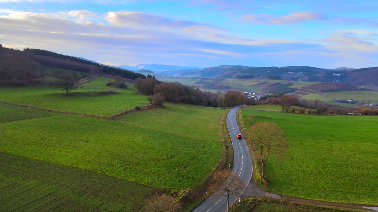 un nuevo día en bruchhausen: una vista aérea de un camión naranja que conduce un camino terrestre con el paisaje verde circundante al amanecer