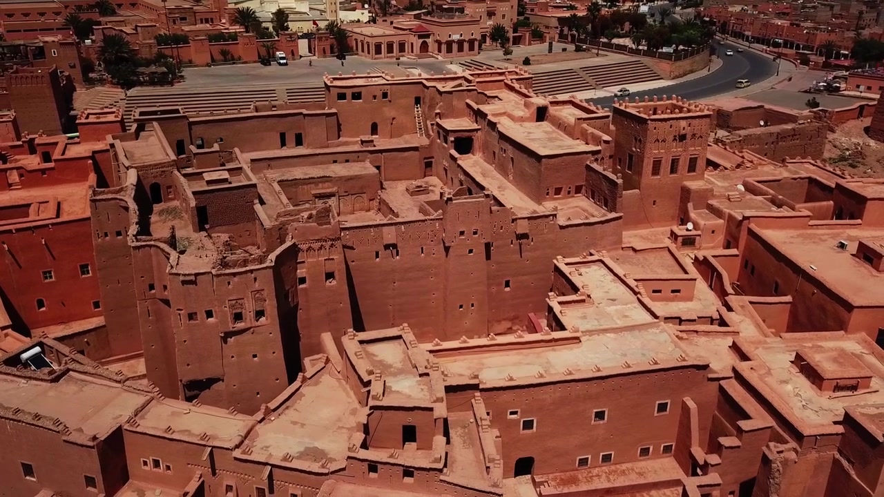 Vista aerea di edifici tradizionali di kasbah che si fondono con le infrastrutture moderne a Ouarzazate, Marocco. Contrasto tra l'architettura storica in adobe e gli elementi urbani contemporanei, ideale per un'esperienza culturale.