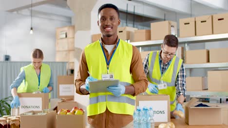 front view of african american male volunteer checking donation list and smiling to the camera in warehouse house