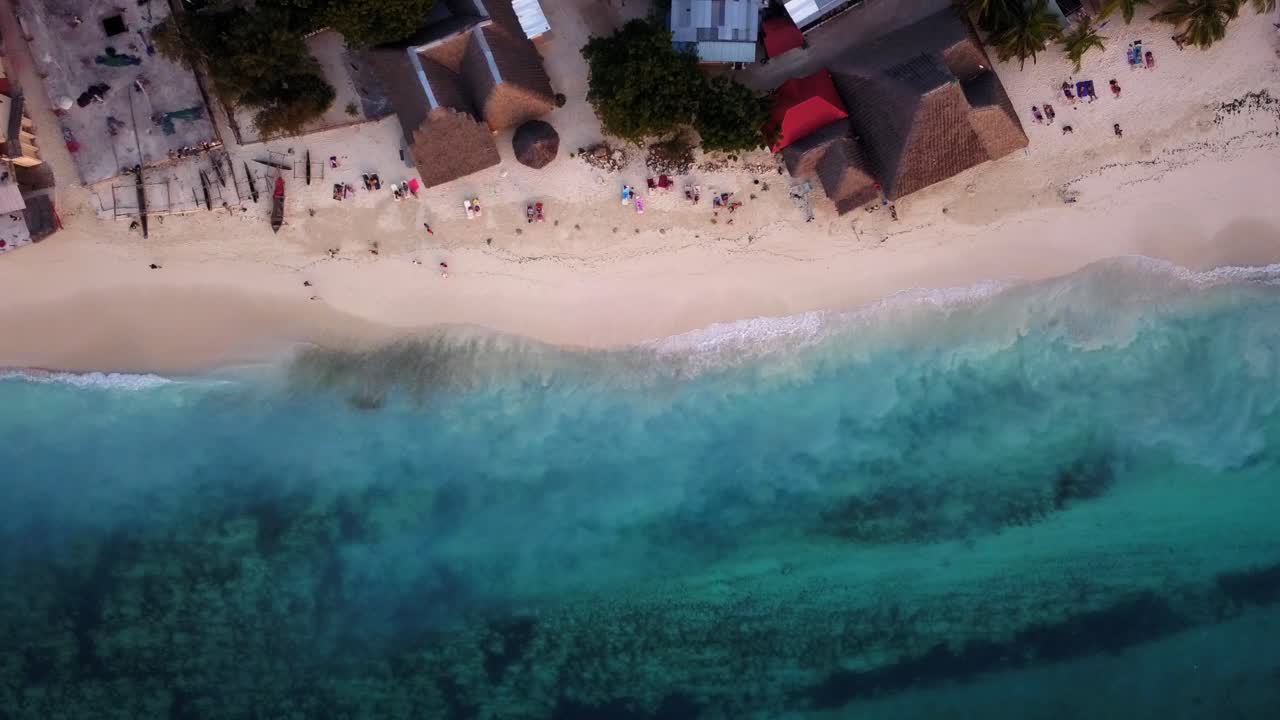 toma aérea de personas caminando y relajándose en la playa de nungwi mientras pequeñas olas rompen en la orilla arenosa de zanzíbar, unguja, isla en tanzania durante la puesta de sol
