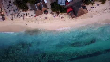 toma aérea de personas caminando y relajándose en la playa de nungwi mientras pequeñas olas rompen en la orilla arenosa de zanzíbar, unguja, isla en tanzania durante la puesta de sol