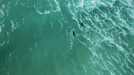 Drone-shot-of-two-surfers-paddling-together-over-waves