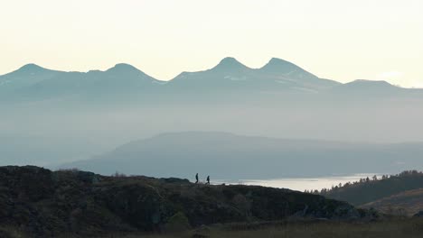 toma de personas caminando sobre una pequeña montaña en la distancia, grandes montañas en el fondo, noruega, molde