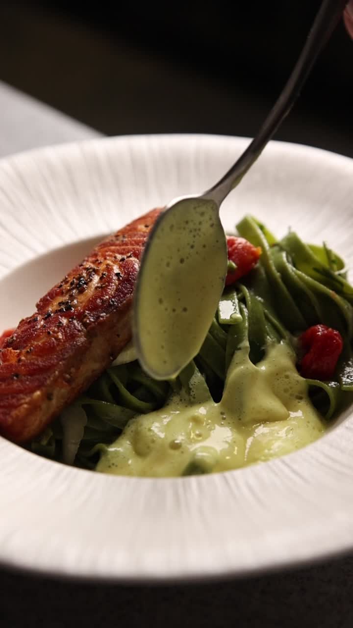 Crema rociada sobre un plato gourmet de salmón y pasta verde