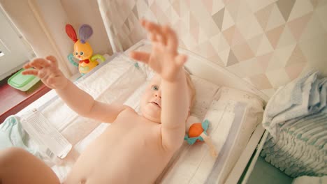 baby girl stretches out hands on the changing mat, wants to get up