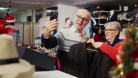 marido y mujer de alto rango en una tienda de moda festiva y adornada hablando con su nieto a través de una videollamada en línea, pidiéndole que elija entre elegantes blazers para comprar como regalo antes del evento familiar de navidad