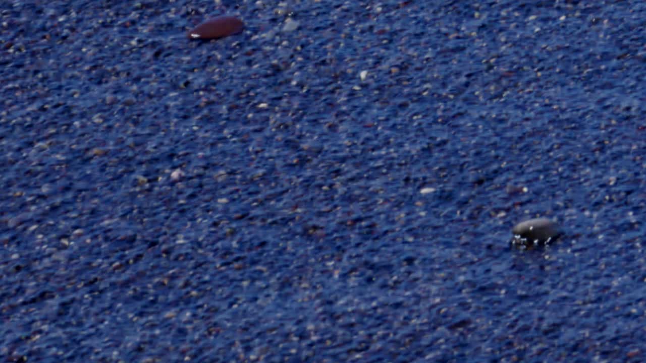 Dark ocean waves crashing over small rocks along scenic volcano black sand beach coastline in Santorini Greece