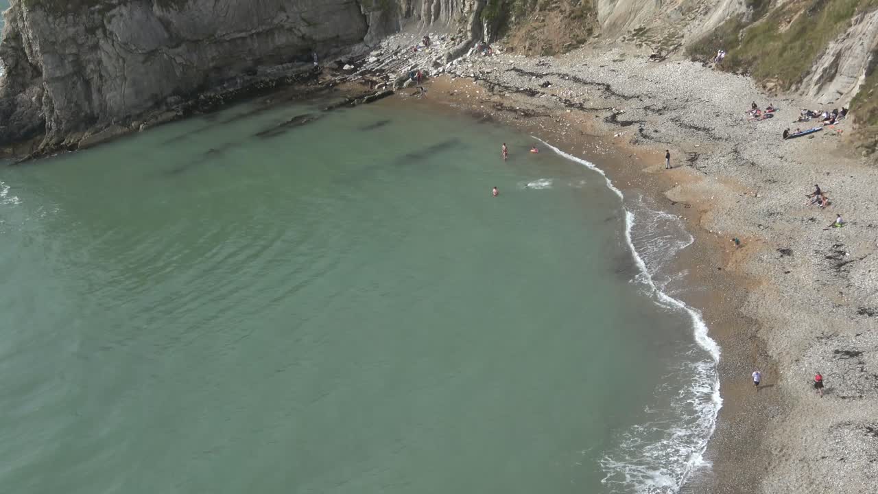 снимок пляжа сверху, несколько стоящих людей и черные водоросли