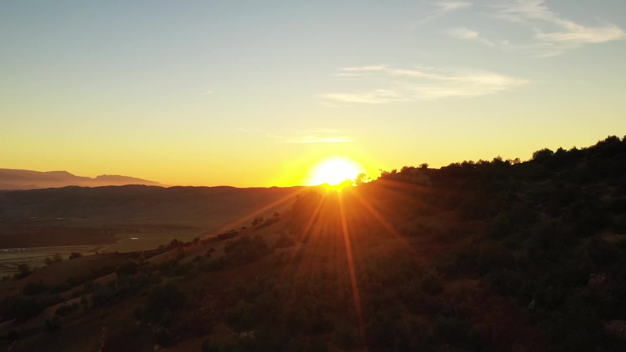 Drohnenaufnahme bei Sonnenuntergang über einem bewaldeten Gebirgskamm mit dramatischen goldenen Sonnenstrahlen im Mittleren Atlas, Marokko, ideal für Reiseinspirationen und Naturdokumentationsprojekte