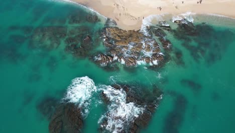 Antena-Mirando-Hacia-Abajo-Sobre-Las-Olas-Rompiendo-Sobre-Rocas-Cerca-De-La-Playa-En-Una-Ubicación-Tropical