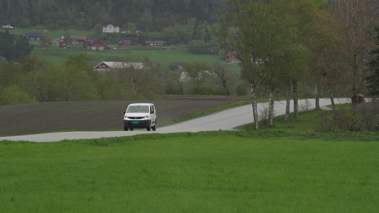 Veicolo bianco che guida per strada attraverso i campi a Indre Fosen, Norvegia.