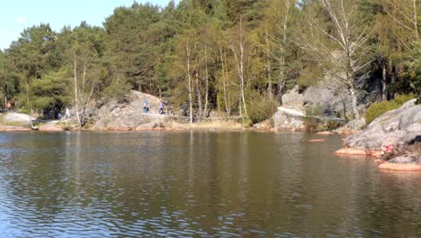 Family-hiking-by-a-lake-while-passing-two-joggers-on-a-sunny-day,-wide-shot