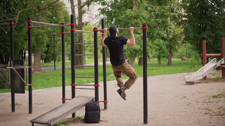 Individual Practicing Pullups In Park Environment, Athlete Performing Pull Exercises With Backpack Nearby In Park, Energetic Workout Session Where Person Executes Pullups Outdoors With Focused Effort