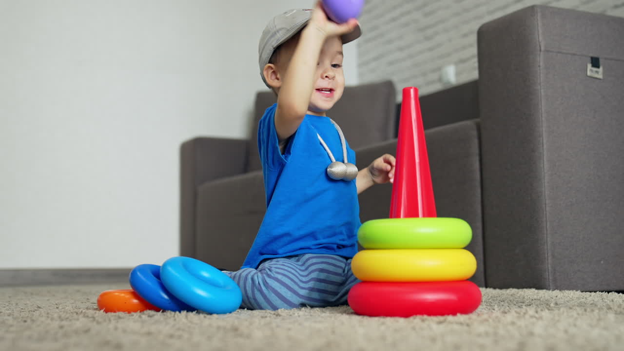 Lovely cute Caucasian toddler playing cheerfully with toy in his room. Energetic kid assembling pyramid.