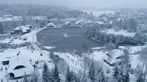 aerial drone forward moving shot over wooden cottages covered with snow beside frozen lakes on a cold winter day