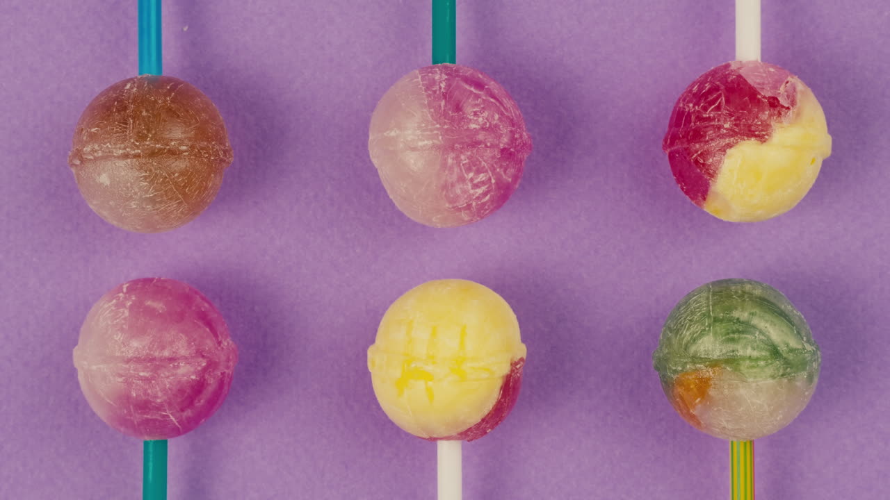 Sweet lollipops with glitter sprinkles on color purple background. Bright texture sugar candies close up top view. Composition of favorite children's summer sweets. Studio shot for shop, supermarket, confectionery