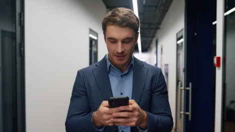 smiling employee texting mobile phone. happy manager walk hallway leave office