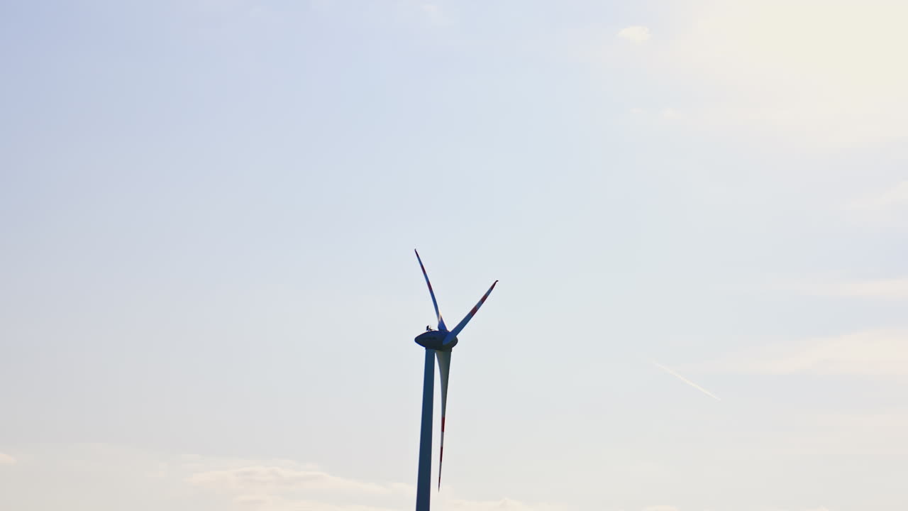 Wind turbine stands tall under blue sky. A wind turbine rotates slowly against a clear sky while harnessing renewable energy near a coastal area