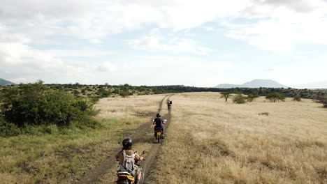 Vista-Aérea-De-4k-De-Motociclistas-Que-Viajan-En-Línea-En-Un-Camino-árido-En-El-Este-De-África