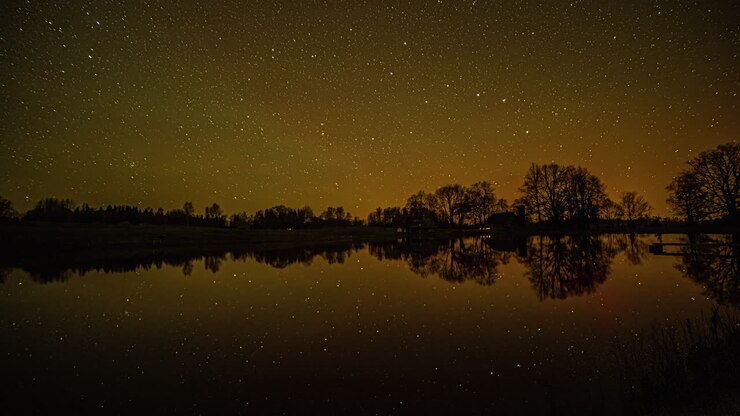 Timelapse di una notte stellata con il movimento delle stelle e il riflesso su un lago scuro con alberi