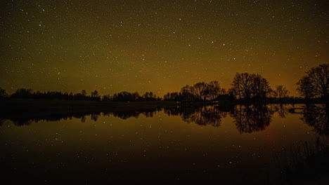 Starry-night-timelapse-with-star-movement-and-reflection-on-a-dark-lake-with-trees